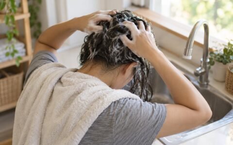 Wanita mengurut syampu ke kulit kepala semasa mencuci rambut di rumah